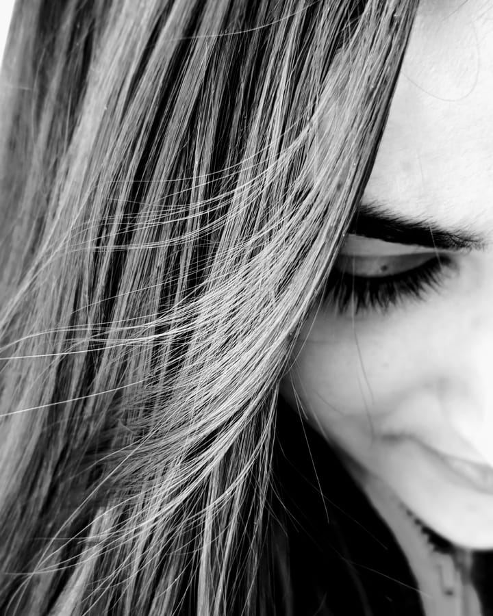 Reverie. A half-face turned down and inward, hair falling across it, the faintest trace of a smile — caught mid-thought. Black and white.
