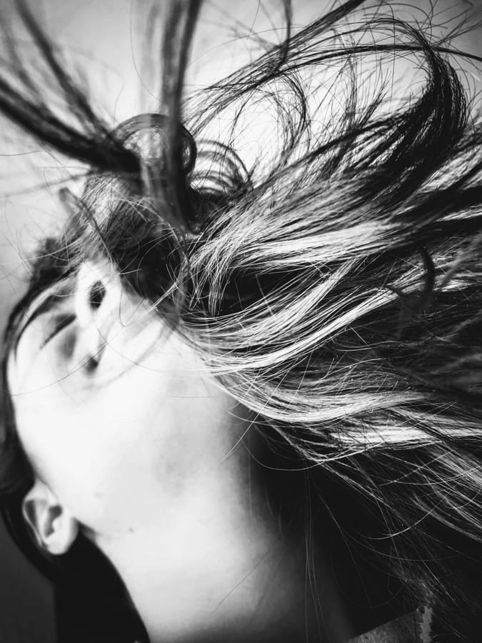 Windswept. Hair thrown across a face by the wind, caught close — all motion and line. Black and white.